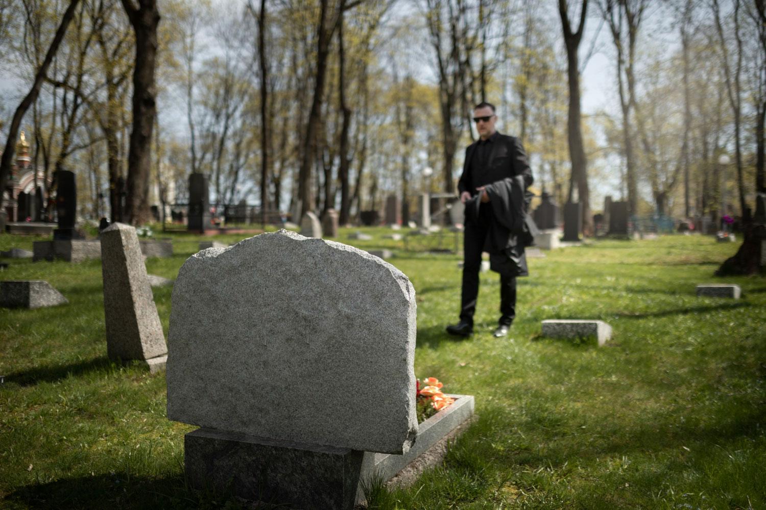 Imagem de um homem visitando o túmulo de um ente querido e lendo mensagem para falecido