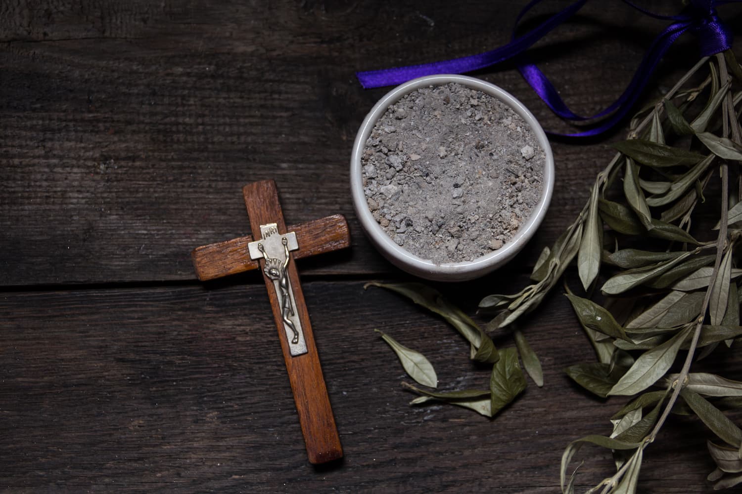 Uma imagem de uma tigela com cinzas, cruz e ramo de oliveira, símbolos da Quarta-Feira de Cinzas