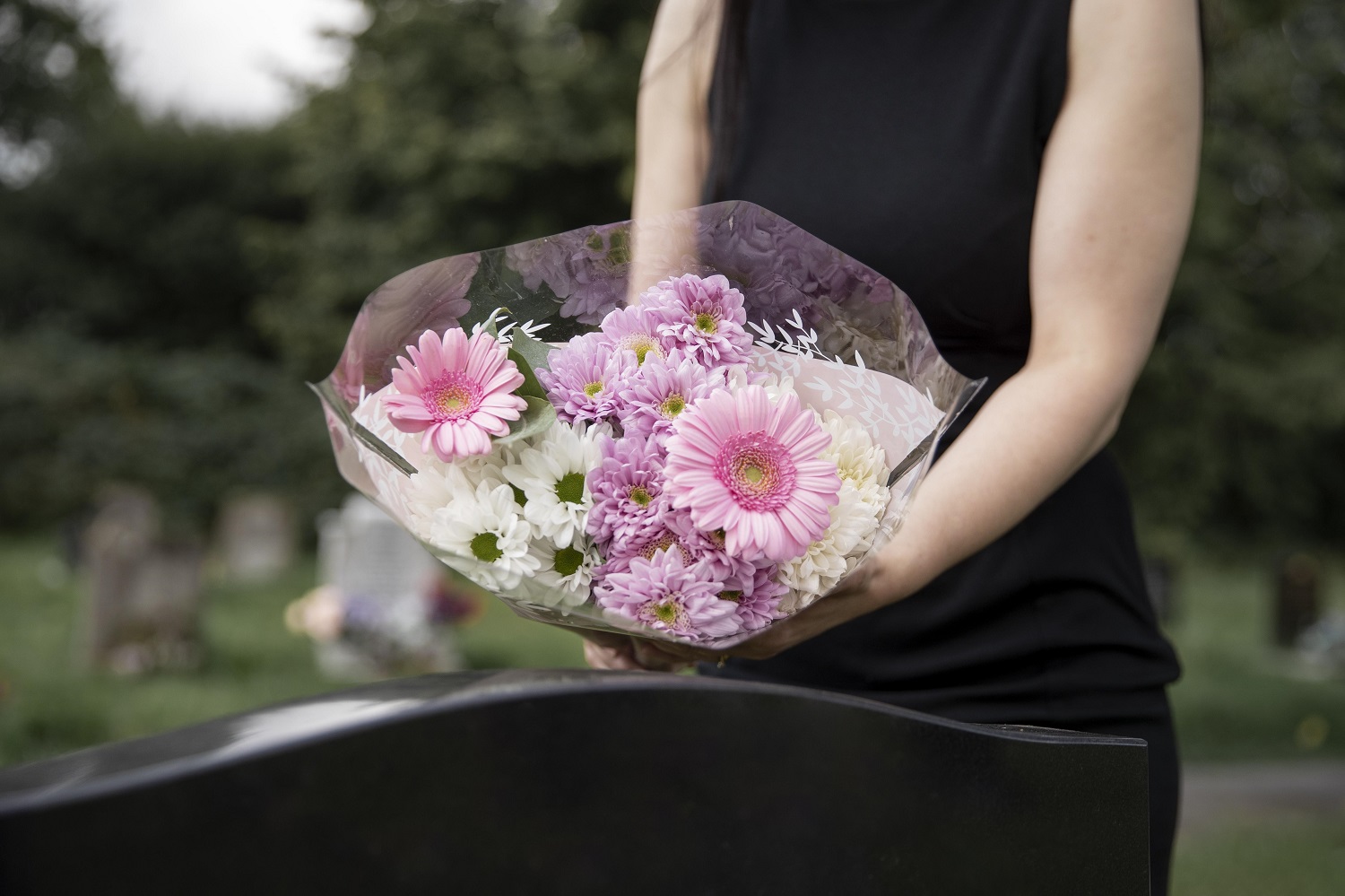 pessoa vestida de preto, com flores na mão prestando as últimas homenagens ao ente querido que faleceu